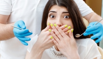 Fearful dental patient covering her mouth with her hands