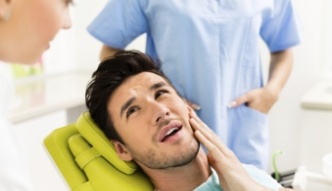 Man holding his cheek in pain while talking to dentist