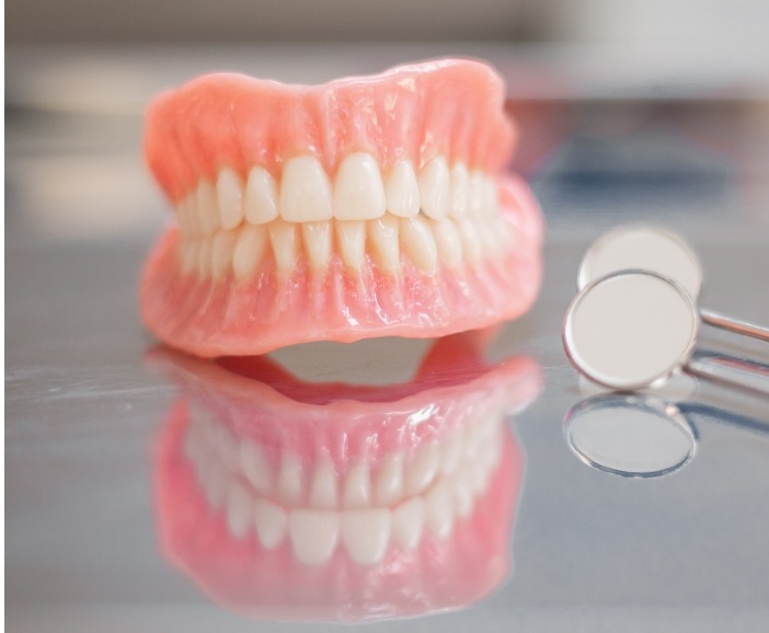 Dentures resting on table next to two dental mirrors