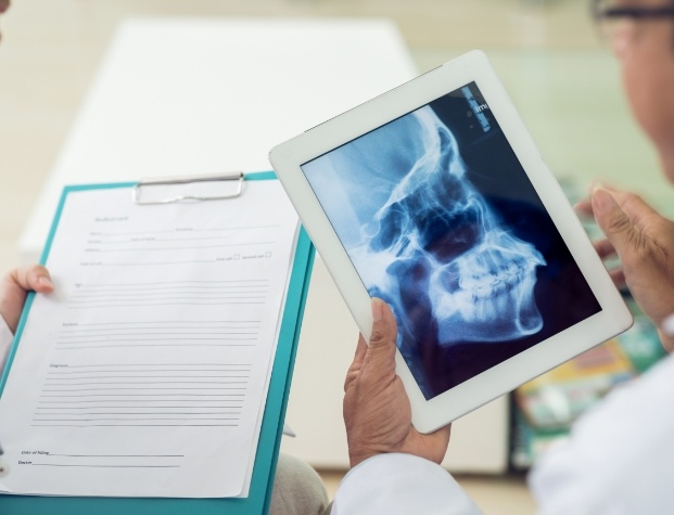 Dentist with clipboard next to dentist with tablet showing x ray of jaw