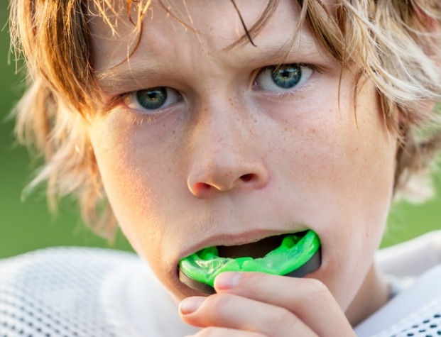 Young boy placing light green mouthguard over his teeth