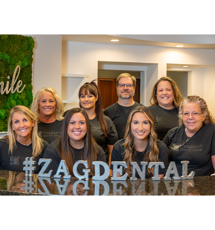 Westerville dental team behind front desk with stand letters that spell out hashtag zag dental